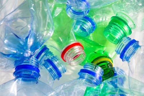A close-up image of several transparent plastic bottles in various shades of blue and green, with some featuring colored screw caps in red, blue, green, and black. The bottles are piled together, showcasing their crinkled textures and clarity, with the caps prominently displayed on top for easy identifications. The background appears blurred, emphasizing the bottles' reflective surfaces and the vivid colors of the caps. The scene suggests the recycling or disposal of plastic waste, relevant to rubbish removal services often provided by companies like Garden Clearance Barbican in the London area, including nearby postal code districts. The image captures the common materials involved in outdoor waste collection, highlighting the importance of proper plastic waste management within urban environments or garden areas requiring clutter clearance.